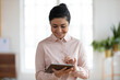 © fizkes - Happy millennial Indian female employee hold modern tablet look at screen work online on gadget. Smiling mixed race woman worker use pad device consult client or customer on web. Technology concept.