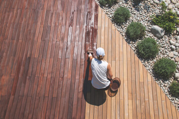 Wood deck renovation treatment, the person applying protective wood stain with a brush, overhead view of ipe hardwood decking restoration process