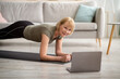 © Prostock-studio - Online sports during covid lockdown. Positive mature lady doing exercises in front of laptop at home, free space