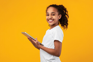 Black girl standing with tablet at yellow studio