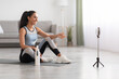 © Prostock-studio - Pretty woman sitting on yoga mat, having video call