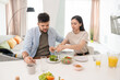 © pressmaster - Young brunette female putting fresh vegetable salad on plate of her husband while both going to have breakfast after cooking it