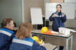 © pressmaster - Young female worker demonstrating usage of respirator while standing by desk in front of colleagues during basics of life safety lesson