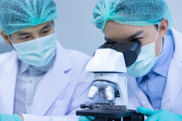 asian man scientist looking sample blood with microscope doing experiment about coronavirus vaccine 