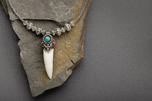 Silver Pendant-amulet With Crocodile Fang. Gray Stone Background, Close-up, Studio Shot.