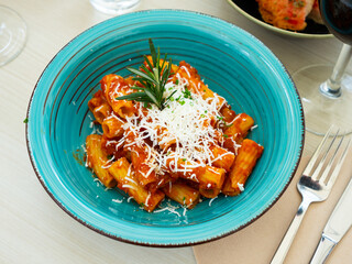 Italian pasta amatricana with tomato sauce and goat cheese on a blue ceramic plate in a restaurant. High quality photo