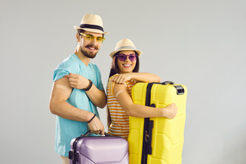 Young people ready for safe summer holiday journey. Studio portrait of happy couple holding travel cases, smiling and showing arms after receiving COVID-19 vaccine. Coronavirus vaccination concept