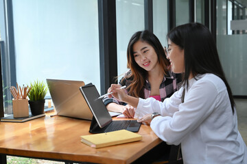 Two young female designers in casual clothes working on project at creative office.