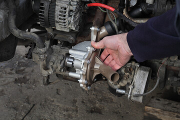 Wall Mural - Car mechanic replacing water pump at modern common rail diesel engine, closeup of workers  hand holding part