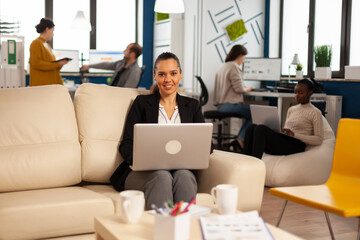 Poster - Manager lady writing on laptop looking at camera smiling while diverse colleagues working in background. Multiethnic coworkers talking about startup financial company in modern business office