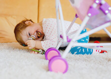 Cute Adorable Baby Girl Crawl And Play With Doll Carriage. Beautiful Toddler Child With Pushing Stroller With Toy At Home. Happy Kid With Two Dolls