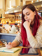 © evafesenuk - A pensive woman with red hair works remotely in a cafe, writes in a diary.