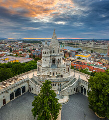 Wall Mural - Budapest, Hungary - Aerial view of the famous Fisherman's Bastion at sunrise with colorful clouds and Parliament building at background. Green trees, blue sky, no people on a sunny summer morning