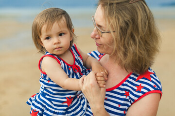 Wall Mural - Happy middle-aged mature grandma and little toddler granddaughter hug together portrait, loving old grandmother granny and cute carefree grandkid girl embrace on beach at summer vacation