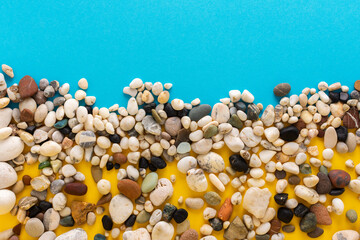 Sea colorful pebbles on a blue and yellow background, copy space, vacation on the sea or ocean, background like sand with water