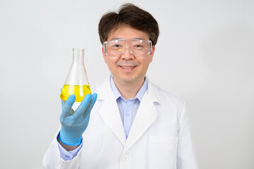 Portrait of a middle-year Asian male scientist wearing a white lab gown and gloves and holding an experimental container in his hand.