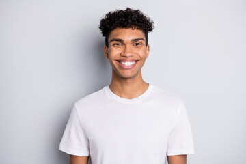 Portrait of brunet optimistic curly guy wear white t-shirt isolated on grey color background