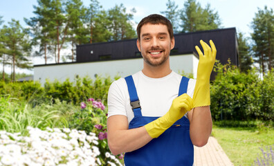 profession, cleaning service and gear concept - happy smiling male worker or cleaner in overall wearing gloves over summer garden background