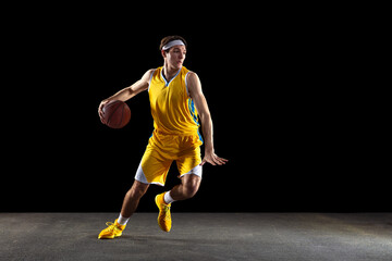 Wall Mural - Young Caucasian basketball player training isolated on black background.