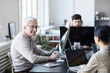 © Seventyfour - Portrait of smiling senior man collaborating with young people in modern office, career change concept, copy space