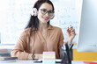 © H_Ko - Woman teacher in headphones looking at computer screen on background of blackboard