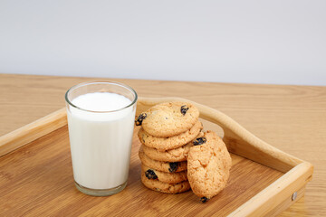 A glass of milk and cookies with raisins on a wooden tray