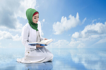 Wall Mural - Asian Muslim woman in a veil sitting and reading the Quran