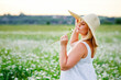 © Elena  - a beautiful plus-size girl in a hat and a white summer dress poses outdoors with camomiles. A plump girl in a meadow with daisies.