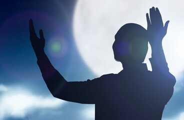 Wall Mural - Silhouette of Muslim man standing while raised hands and praying