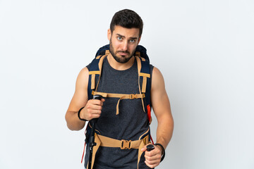 Young mountaineer man with a big backpack and trekking poles isolated on white background pleading