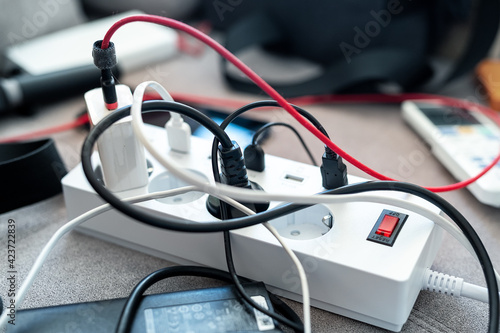 Obraz Dibond Overloaded power socket plug extendion at home. Tangled cords of home appliances and chargins gadgets mess