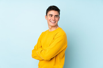 Teenager caucasian handsome man isolated on purple background with arms crossed and happy