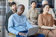 © Seventyfour - Diverse group of business people sitting on chairs in audience and listening at meeting or seminar, focus on African-American man with laptop in foreground