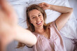 © Dragana Gordic - Beautiful woman lying on bed and taking selfie. Self top above view portrait of pretty, brunette, charming, cute, glad, pleased, positive girl. Young cheerful woman taking selfie portrait