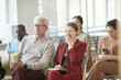 © Seventyfour - Diverse group of business people sitting on chairs in audience and listening at meeting or seminar, focus on young businesswoman yawning in foreground
