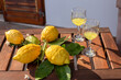 Lemons with leaves, lemonade or limoncello in a glass glass, on a wooden table on the terrace.