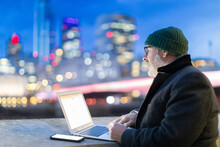 Man Working On Laptop In City At Night, London, UK