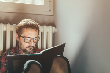 Wall Mural - Casual mid adult male with eyeglasses enjoys reading a book at home