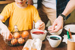© Anna - Easter day. Cropped Father and son painting eggs on wooden background. Family sitting in a kitchen. Preparing for Easter, creative homemade decoration.