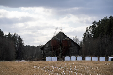 A large barn in the Latvian countryside with two large rusty metal barrels and white rolls of acid in the foreground