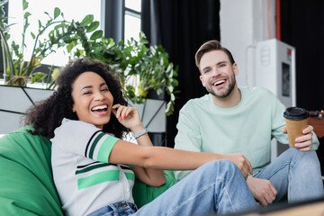 cheerful multicultural business colleagues looking at camera while resting in office lounge zone