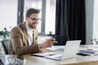© LIGHTFIELD STUDIOS - cheerful businessman pointing at laptop while working on blurred foreground