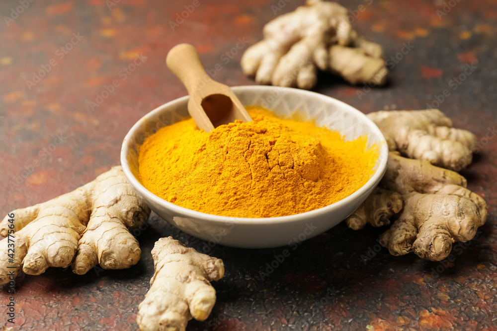 Bowl and scoop with turmeric powder on grunge background