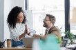 © LIGHTFIELD STUDIOS - Smiling interracial business people giving high five near devices in office