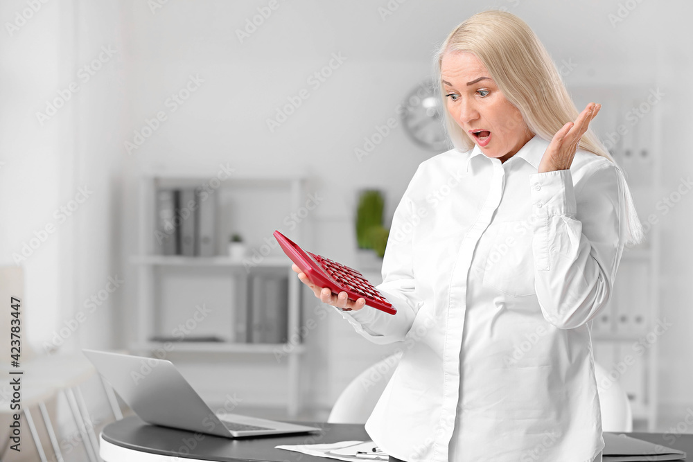 Stressed mature accountant with calculator working in office