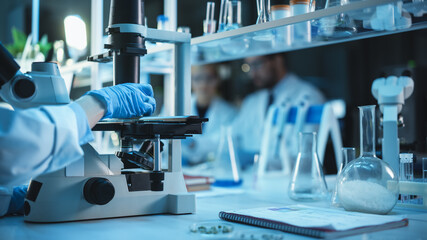 Wall Mural - Close Up Shot of a Medical Research Scientist in Blue Gloves Conducting Biological Experiments Under a Microscope in a Biological Applied Science Laboratory.