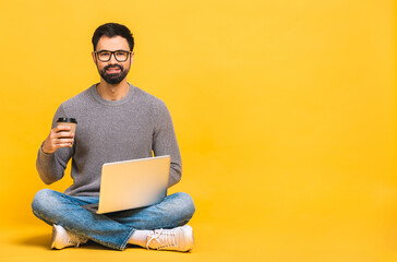 portrait of a happy young bearded man in casual holding laptop computer while sitting on a floor iso