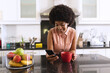 © wavebreak3 - African american woman in kitchen drinking coffee and using smartphone