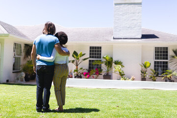 Diverse couple embracing in front of house on sunny garden terrace