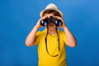 © Med Photo Studio - Little boy in a yellow t-shirt holding a binocular and watching on a blue background.